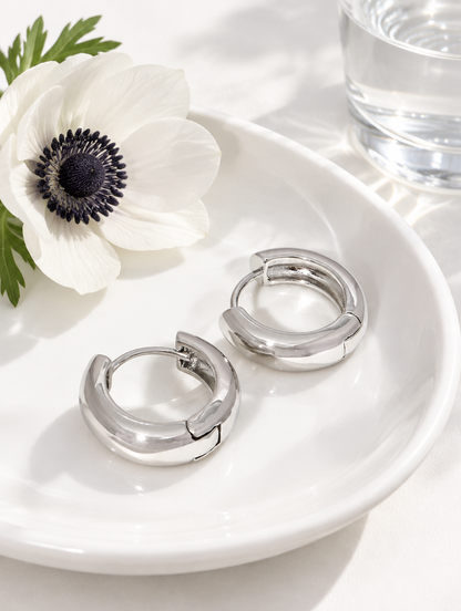 Silver-tone chunky huggie hoop earrings in a styled still life with props