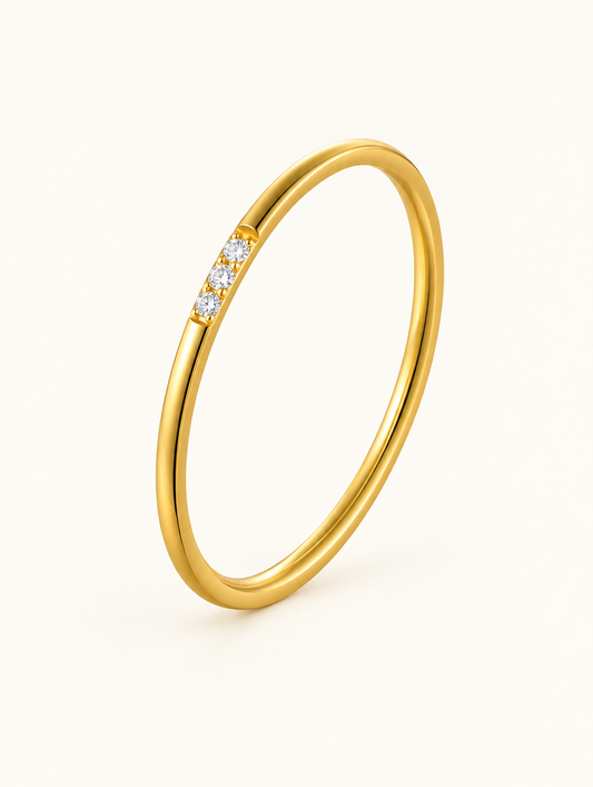 Thin gold stacking ring with three zirconia stones on a neutral background
