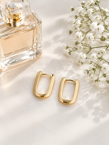 Gold-plated rounded rectangle huggie earrings in a styled still life with props