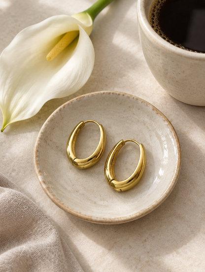 Slim gold-tone elongated oval hoop earrings in a styled still life with props
