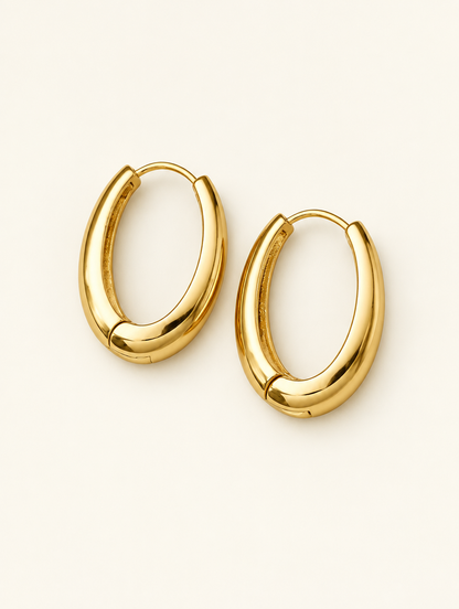 Pair of slim gold-tone elongated oval hoop earrings on a warm off-white background