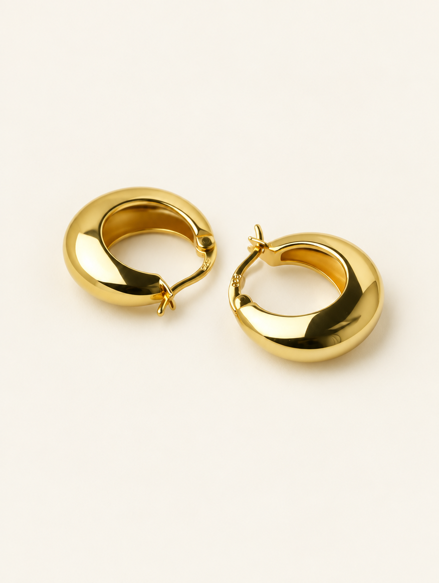 Pair of gold-tone thick rounded hoop earrings on a warm off-white background