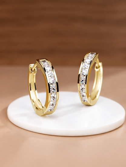 Gold princess-cut zirconia hoop earrings lying flat on a soft styled surface