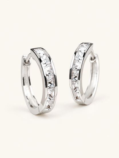 Pair of silver princess-cut zirconia hoop earrings on a warm off-white background