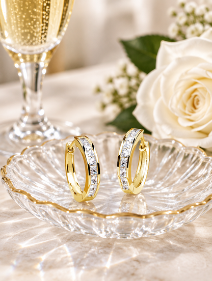 Gold princess-cut zirconia hoop earrings in a styled still life with props