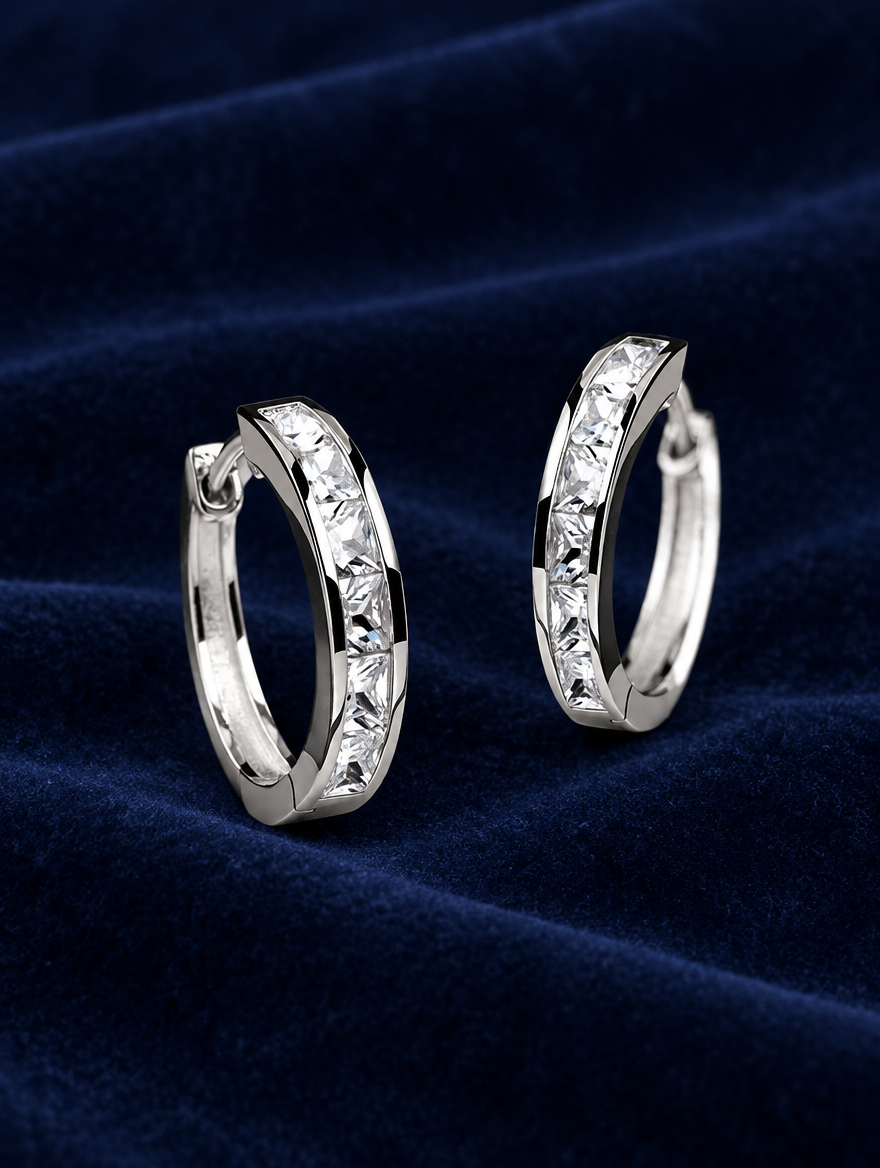 Silver princess-cut zirconia hoop earrings lying flat on a soft styled surface