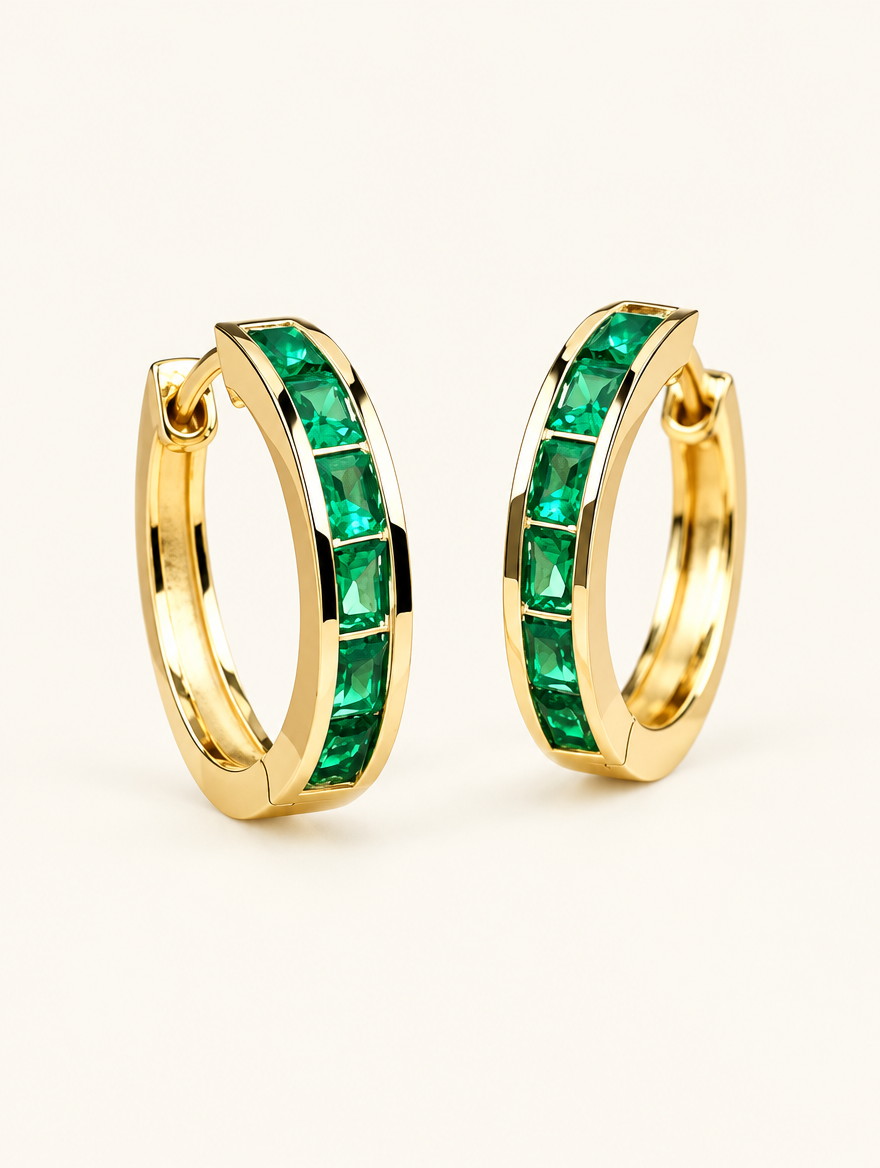 Pair of gold emerald-green zirconia hoop earrings on a warm off-white background