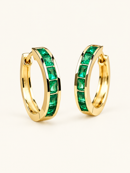 Pair of gold emerald-green zirconia hoop earrings on a warm off-white background