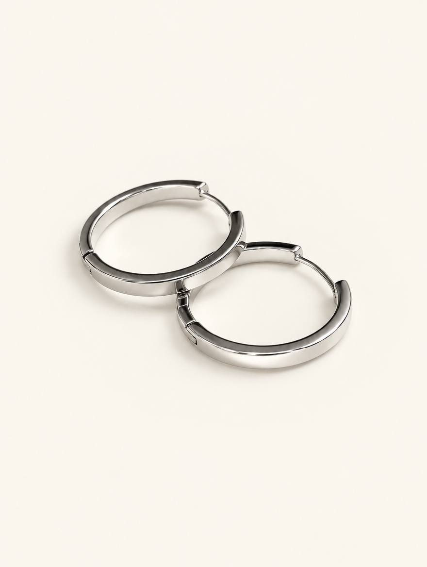Pair of classic silver-tone round hoop earrings on a warm off-white background