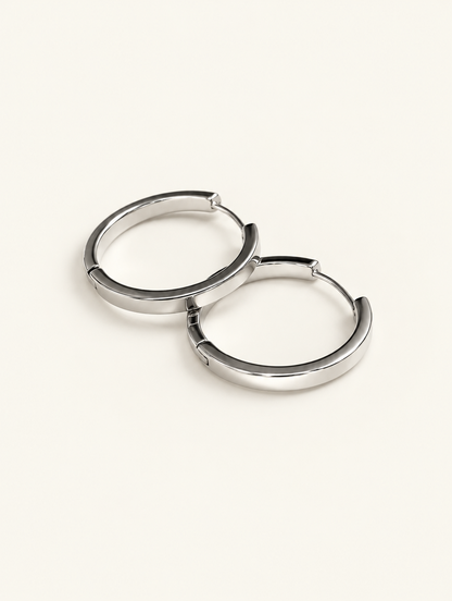 Pair of classic silver-tone round hoop earrings on a warm off-white background