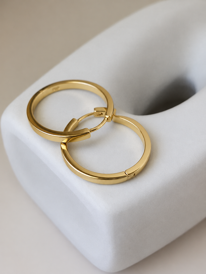 Classic gold-tone round hoop earrings lying flat on a soft styled surface
