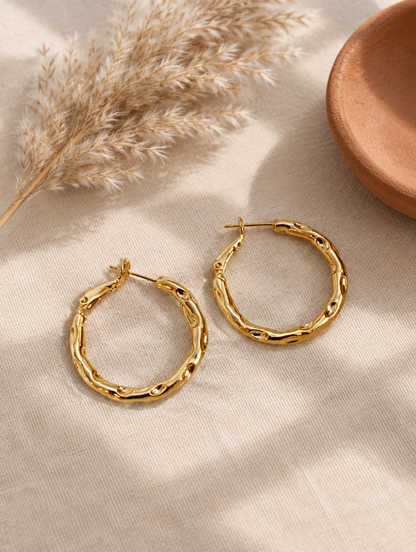 Gold-tone textured twisted hoop earrings in a styled still life with props