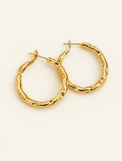 Pair of gold-tone textured twisted hoop earrings on a warm off-white background