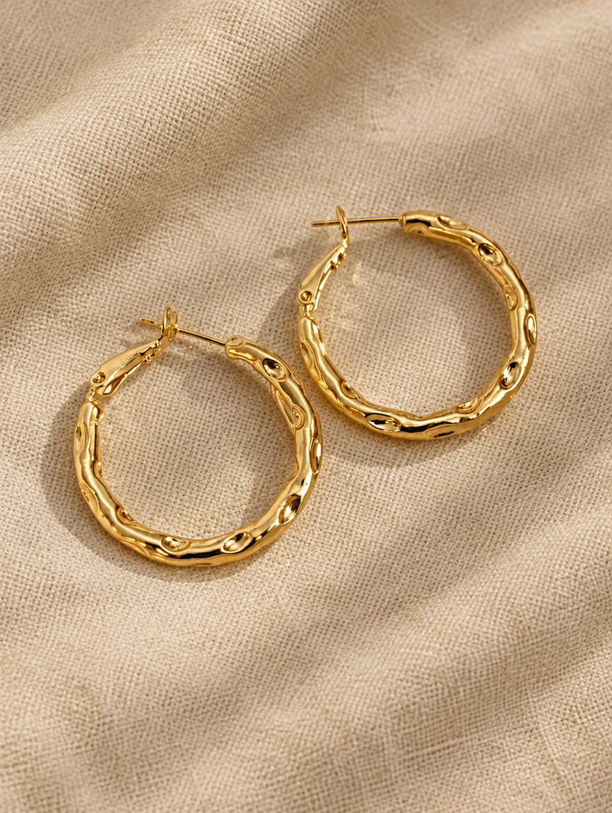 Gold-tone textured twisted hoop earrings lying flat on a soft styled surface