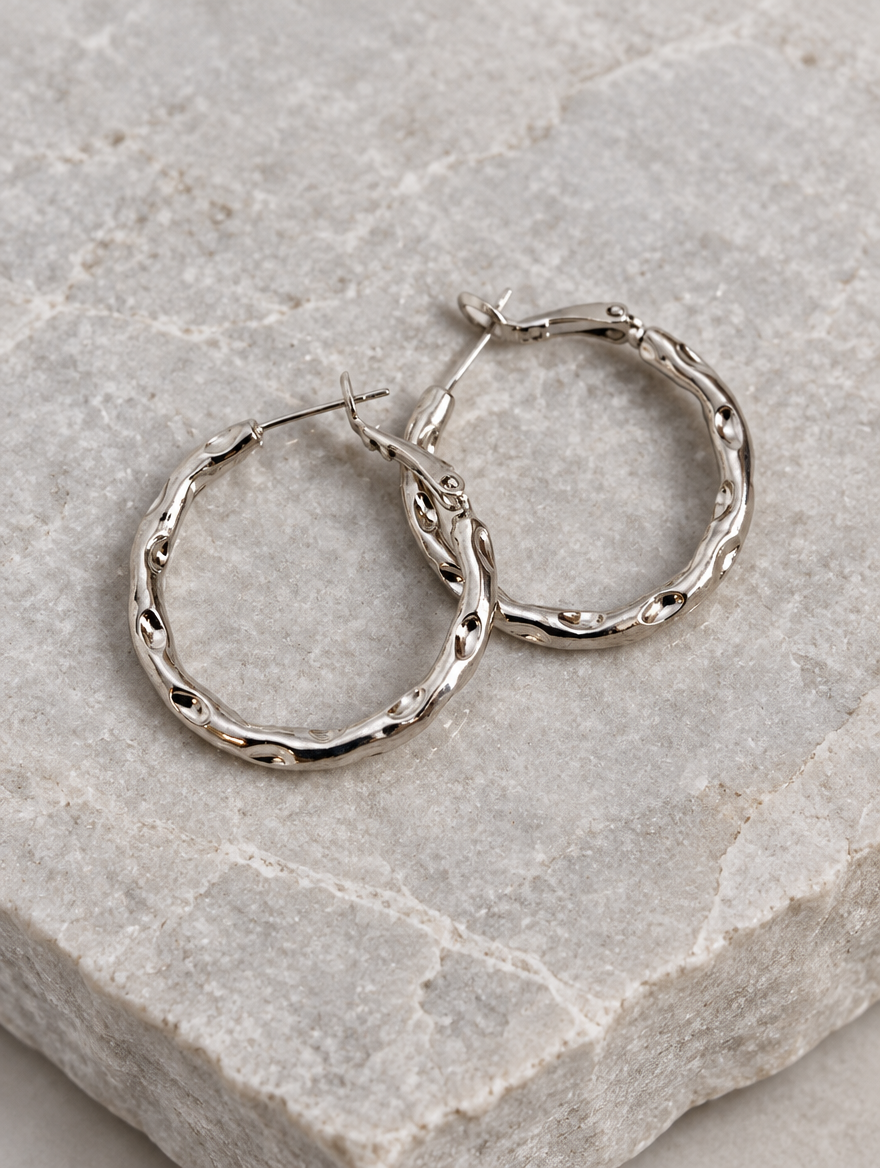Silver-tone textured twisted hoop earrings lying flat on a soft styled surface