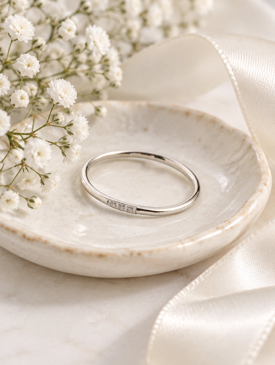 Thin silver stacking ring with three zirconia stones in a small dish with styling props