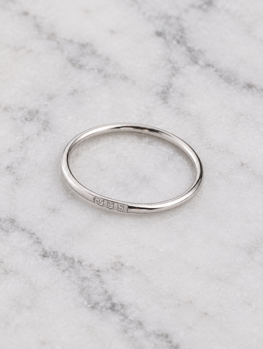 Thin silver stacking ring with three zirconia stones resting on a soft textured surface