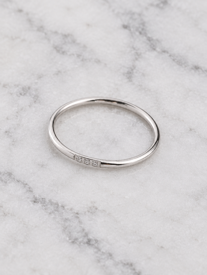 Thin silver stacking ring with three zirconia stones resting on a soft textured surface