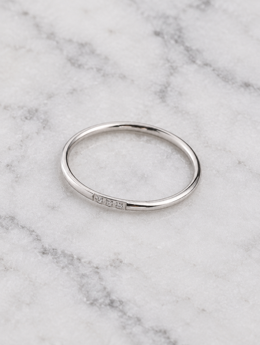 Thin silver stacking ring with three zirconia stones resting on a soft textured surface