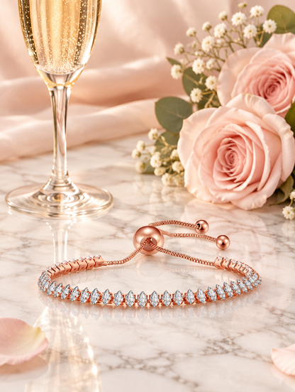 Rose gold slider bracelet beside a champagne flute and blush roses on marble
