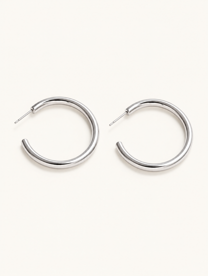 Pair of silver open c-shape hoop earrings on a warm off-white background