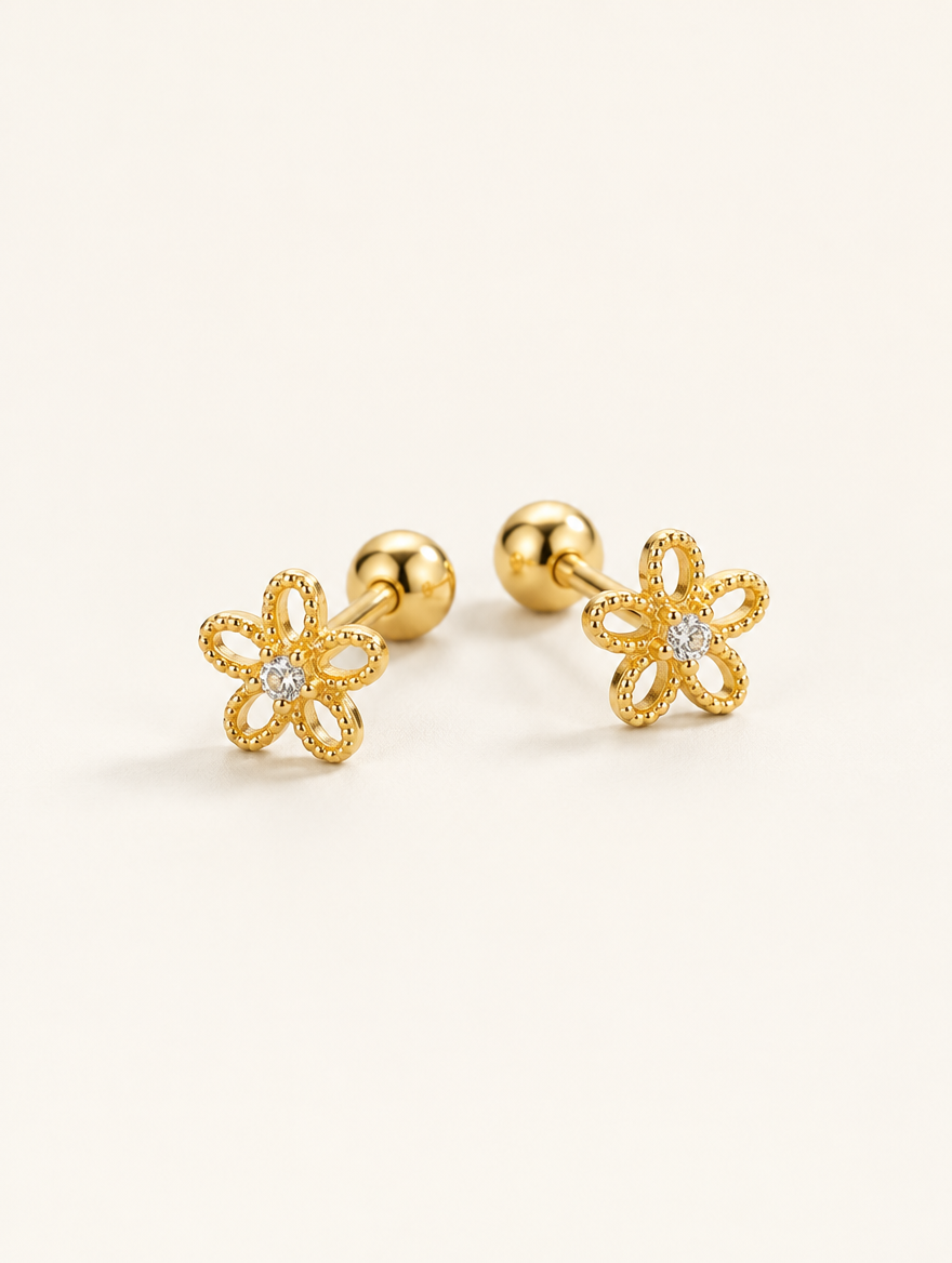 Pair of gold flower stud earrings on a warm off-white background
