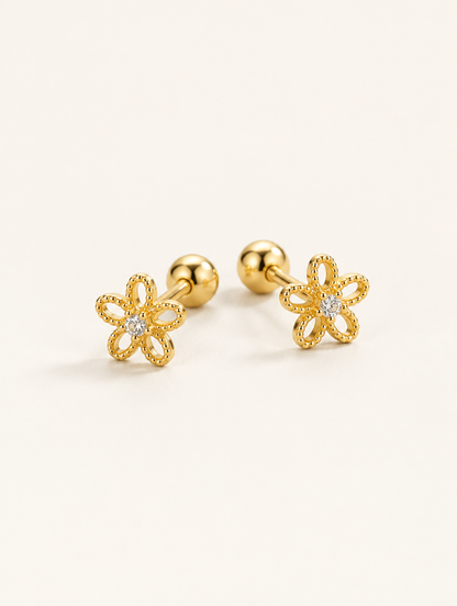 Pair of gold flower stud earrings on a warm off-white background
