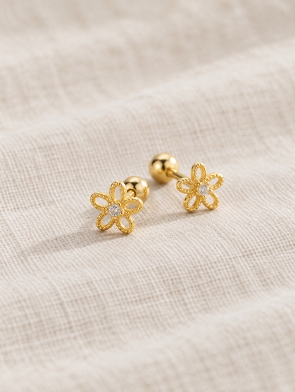 Gold flower stud earrings lying flat on a soft styled surface