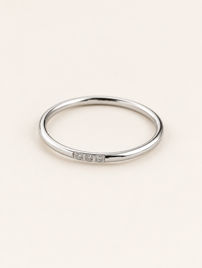 Thin silver stacking ring with three zirconia stones on a neutral background