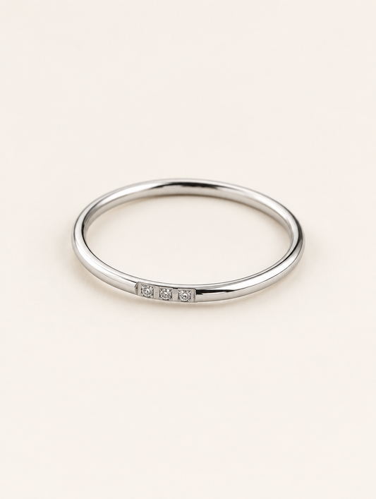 Thin silver stacking ring with three zirconia stones on a neutral background