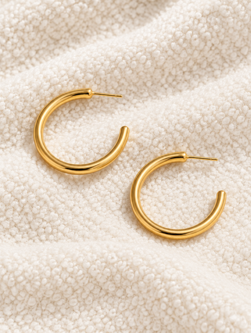 Gold open c-shape hoop earrings lying flat on a soft styled surface