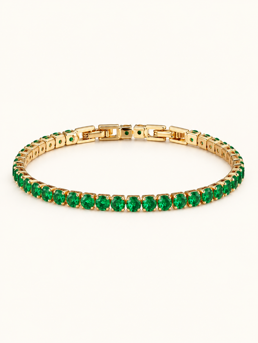 Gold tennis bracelet with emerald green zirconia stones on a neutral background