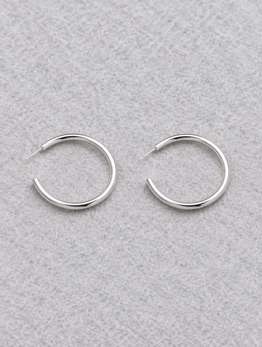 Silver open c-shape hoop earrings lying flat on a soft styled surface