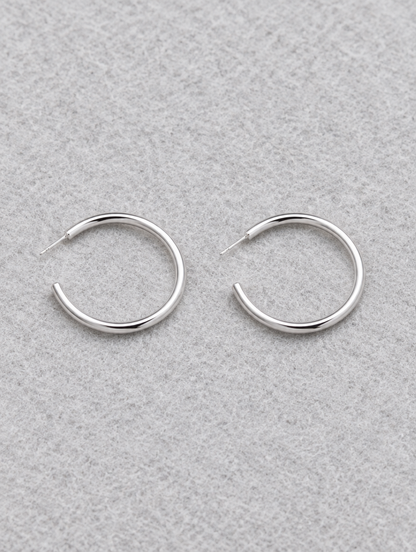 Silver open c-shape hoop earrings lying flat on a soft styled surface