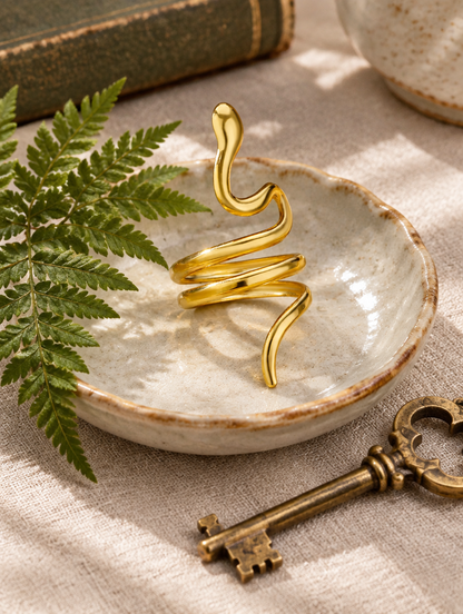 Gold snake coil ring in a small dish with styling props