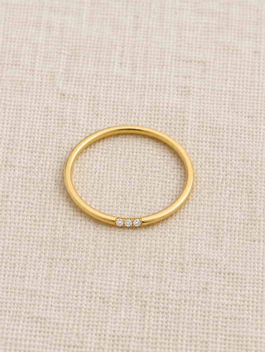 Thin gold stacking ring with three zirconia stones resting on a soft textured surface