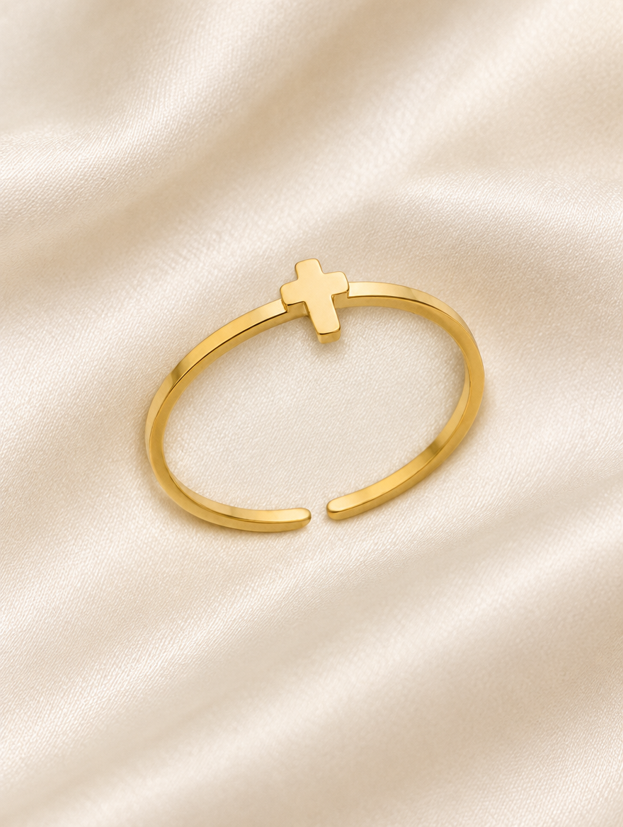 Thin gold cross ring resting on a soft textured surface
