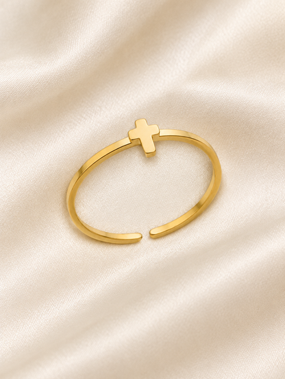 Thin gold cross ring resting on a soft textured surface