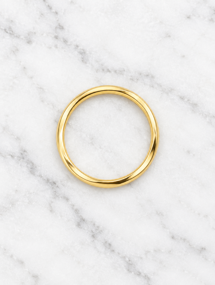 Thin gold polished band ring resting on a soft textured surface