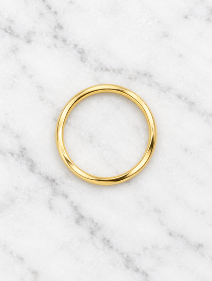 Thin gold polished band ring resting on a soft textured surface