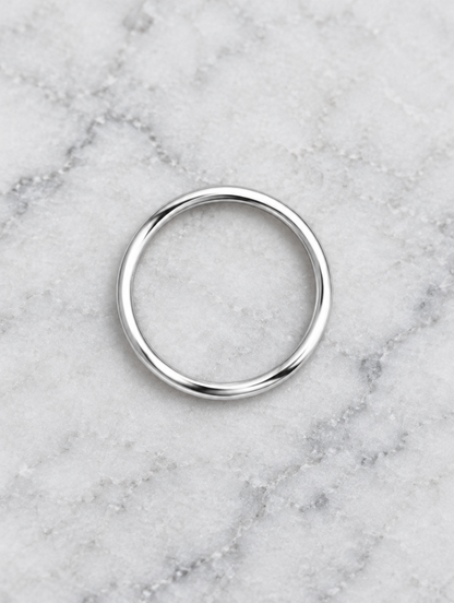 Thin silver polished band ring resting on a soft textured surface