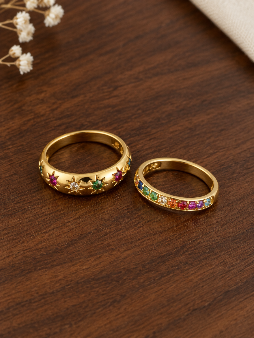 Set of two gold rainbow zirconia and star rings resting on a soft textured surface