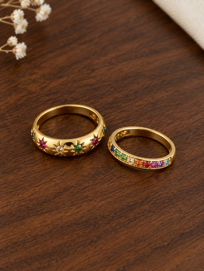 Set of two gold rainbow zirconia and star rings resting on a soft textured surface