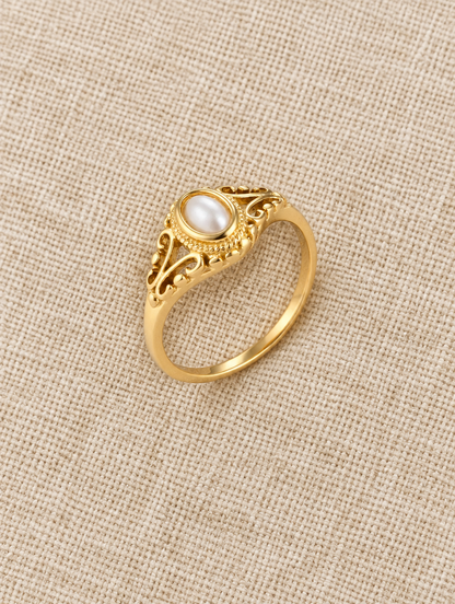 Gold vintage-style pearl ring resting on a soft textured surface
