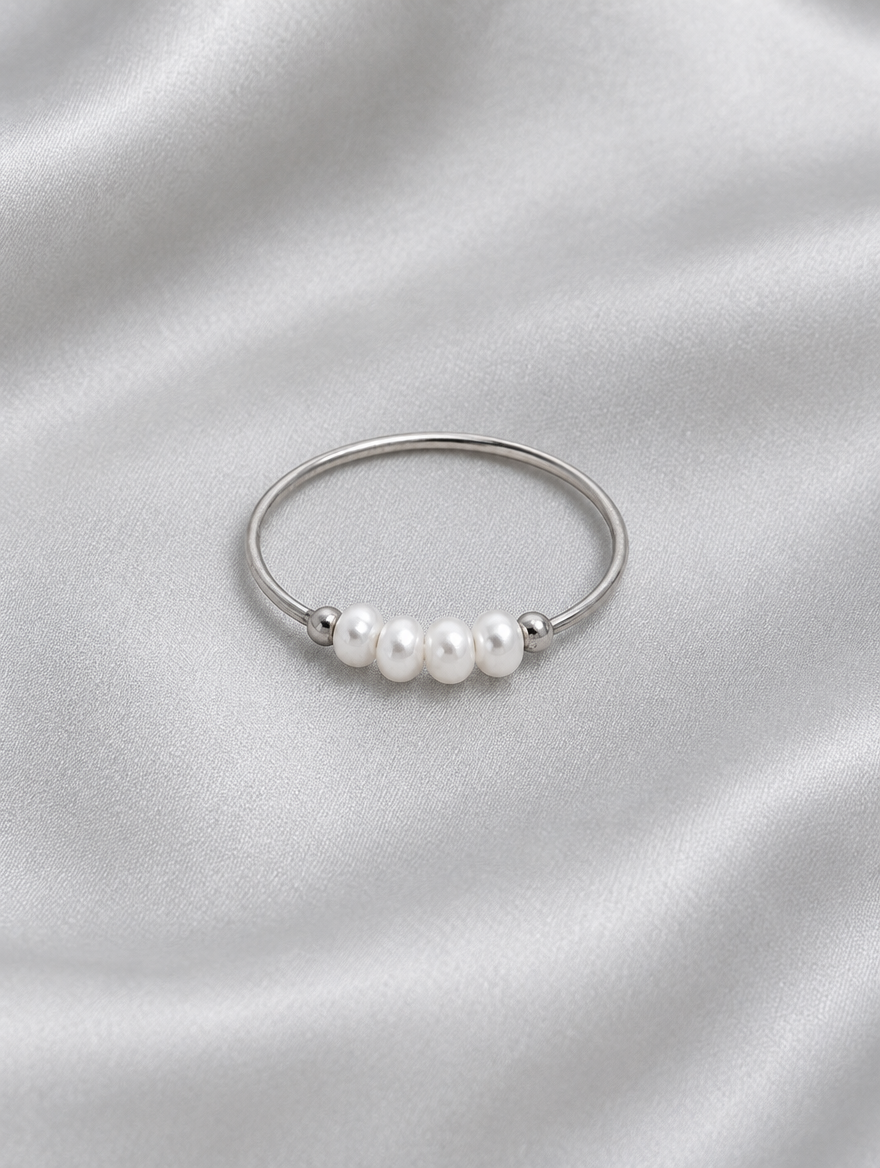 Silver three pearl band ring resting on a soft textured surface