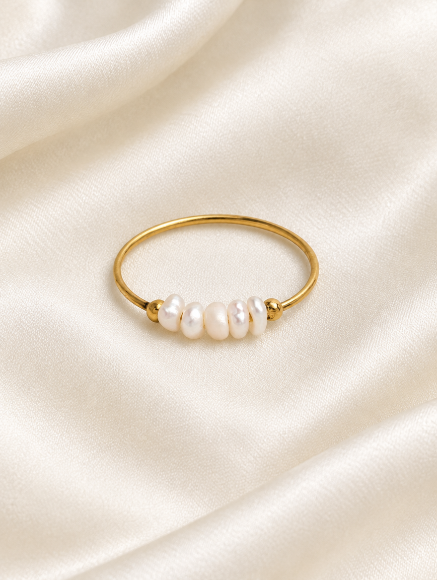 Gold three pearl band ring resting on a soft textured surface