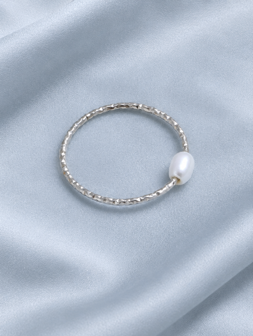 Thin silver twisted band ring with a pearl resting on a soft textured surface
