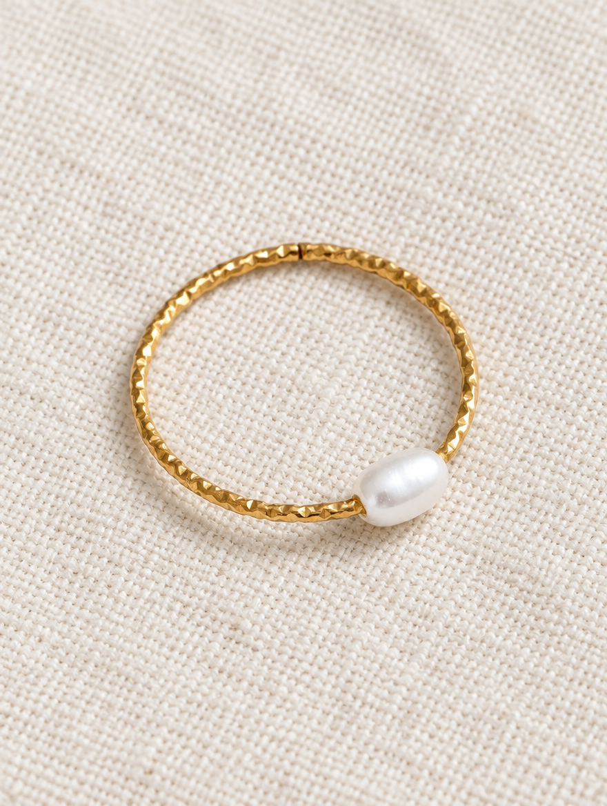 Thin gold twisted band ring with a pearl resting on a soft textured surface