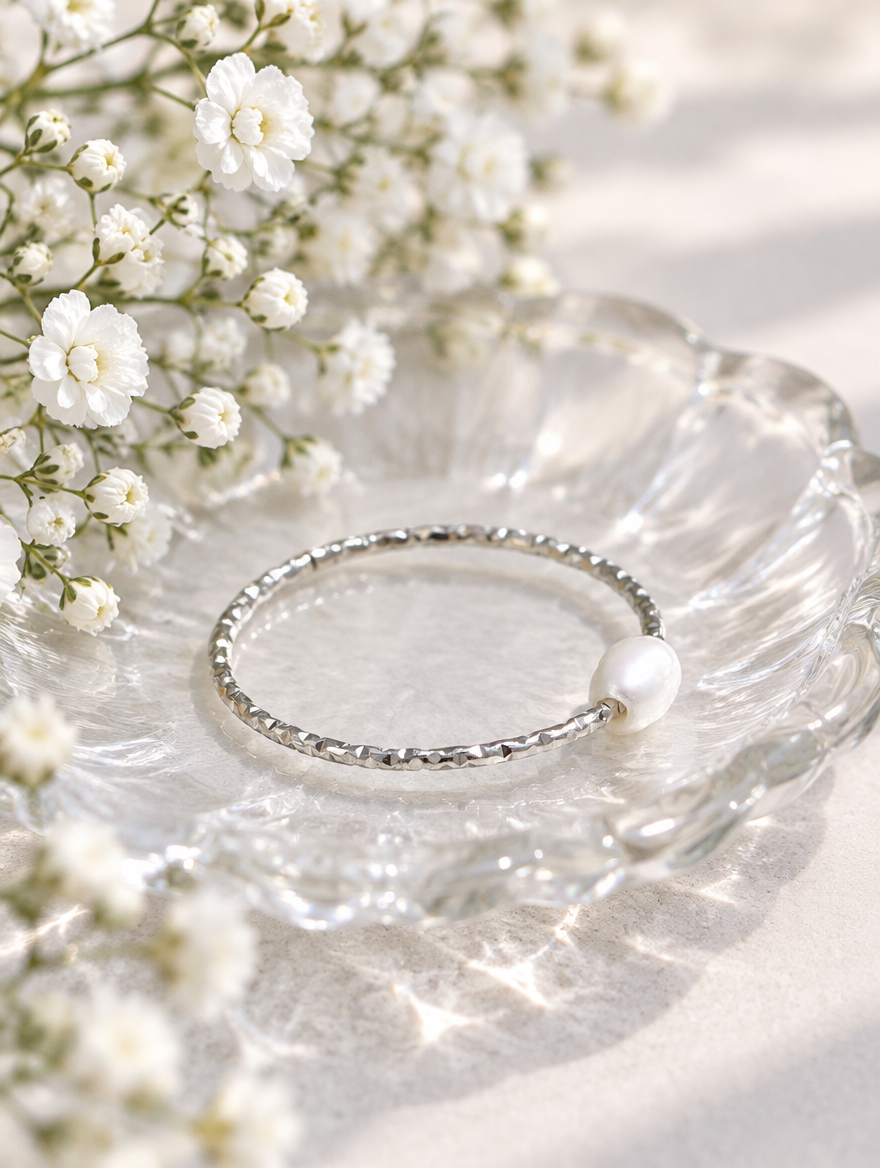 Thin silver twisted band ring with a pearl in a small dish with styling props