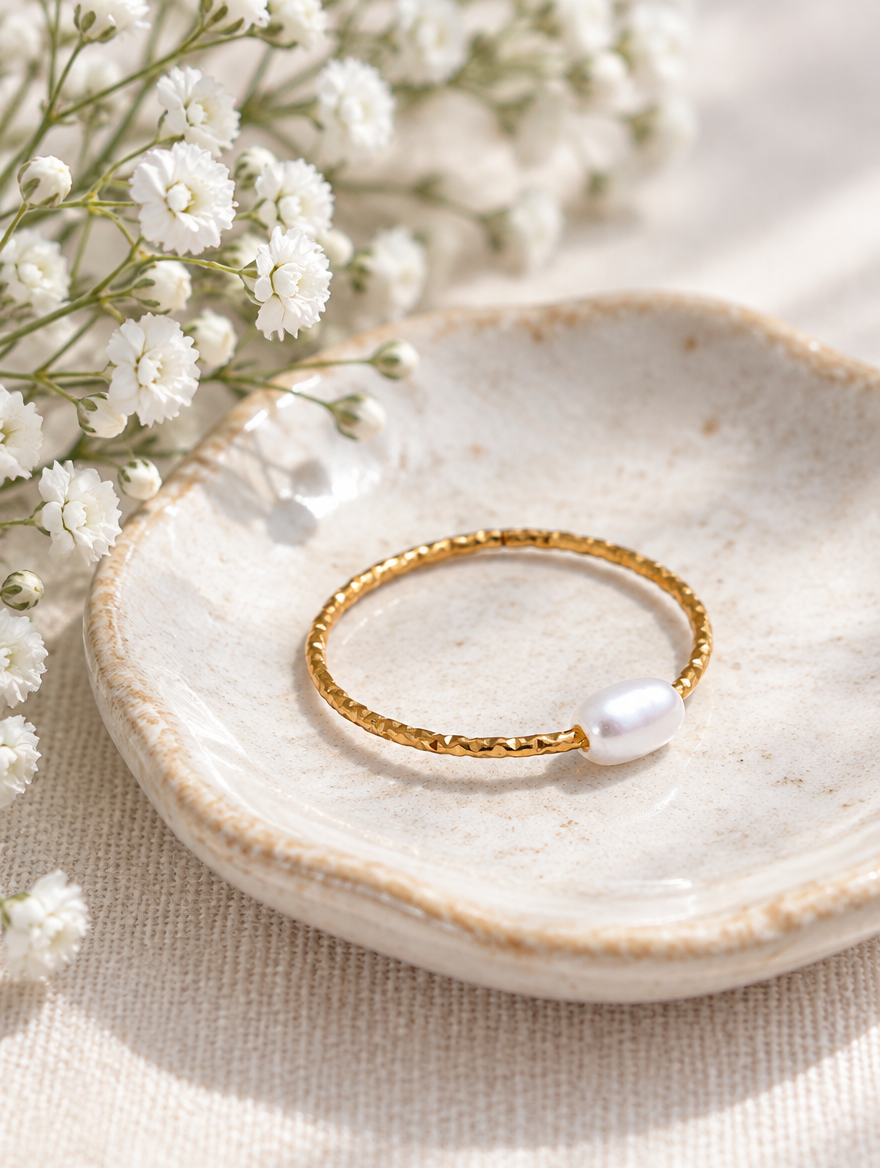 Thin gold twisted band ring with a pearl in a small dish with styling props